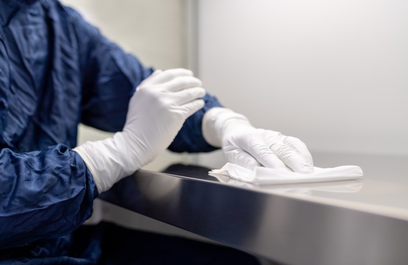 Profissional com equipamento de proteção higienizando superfície