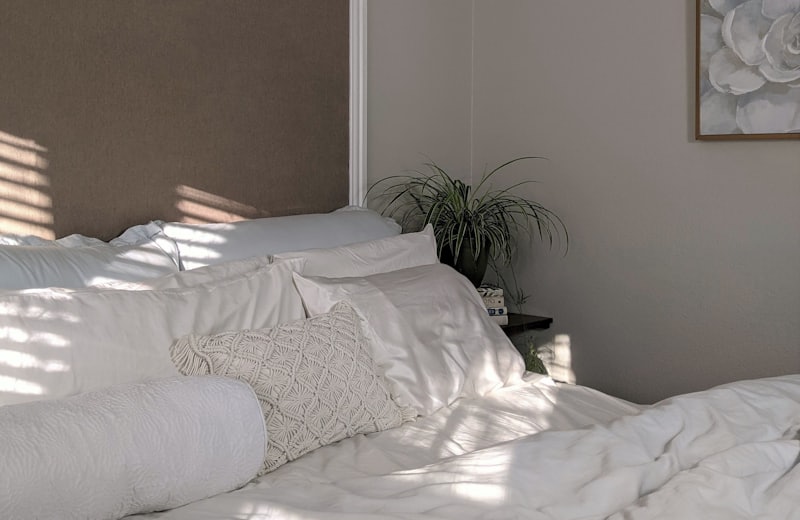 Cama arrumada com roupa de cama branca em quarto claro